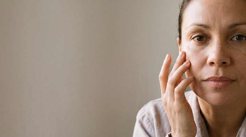 Woman gently touching her cheek in soft winter light, checking in with her skin