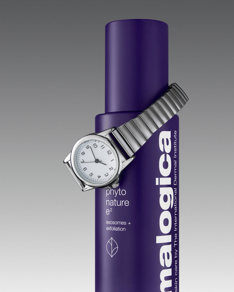 Silver wristwatch wrapped around a purple Dermalogica Phyto Nature e² bottle, featuring product text that highlights "exosomes + exfoliation" on a grey gradient background.